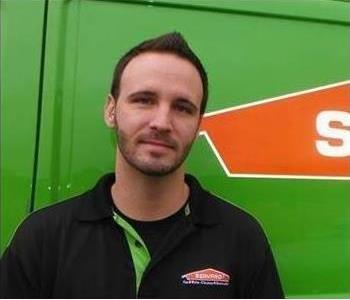 A man with a back polo on standing in front of a SERVPRO vehicle. 